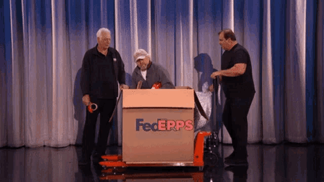three men are standing around a fedex box on a stage