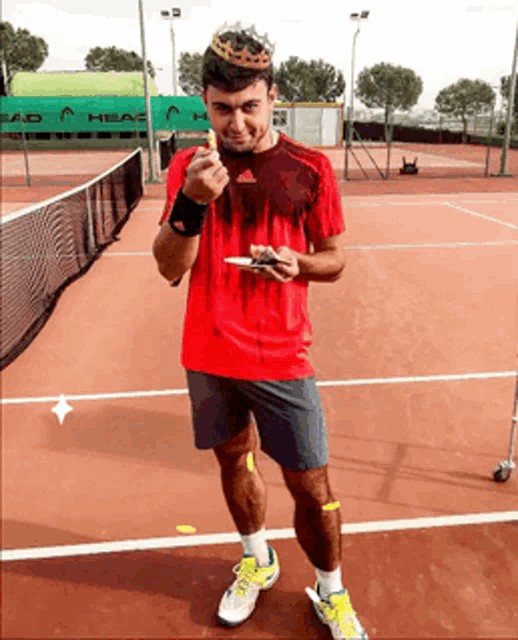 a man standing on a tennis court wearing a crown and holding a plate of food