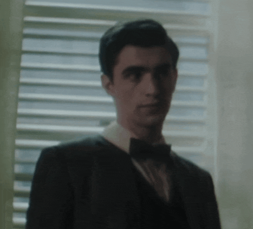 a man in a tuxedo and bow tie stands in front of a window