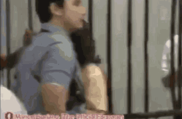 a man in a blue shirt is smoking a cigarette in a cell