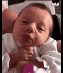 a close up of a baby making a funny face while being held by a person .