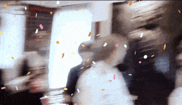 a blurred image of people standing in a room with confetti falling from the ceiling
