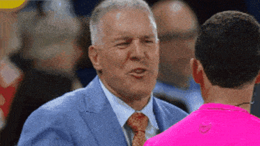 a man in a suit and tie is talking to a man in a pink shirt