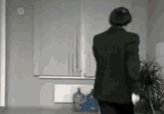 a man in a suit is walking in a room with a plant .