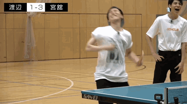 two men are playing ping pong in a gym and the score is 1-3