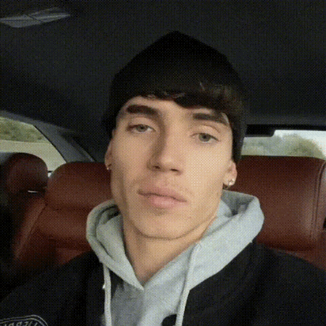 a young man is sitting in the back seat of a car wearing a hoodie and a beanie .