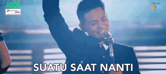 a man singing into a microphone with the words " uatu saat nanti " below him