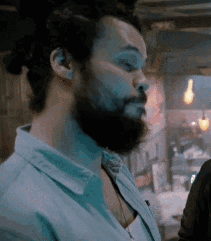 a man with a beard and a bun in his hair is standing in a room .