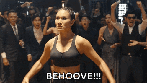 a woman in a black sports bra stands in front of a crowd and says beholde