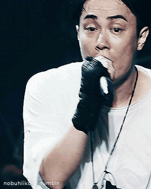 a man wearing gloves is singing into a microphone with the name nobuhiiko tumblr written below him