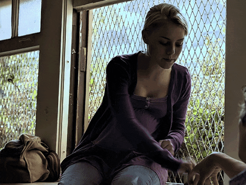 a woman in a purple shirt sits in front of a chain link fence