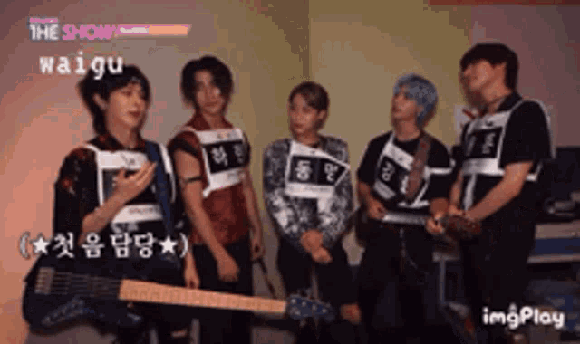a group of young men are standing in a room and one of them is holding a guitar with the name waigu on it
