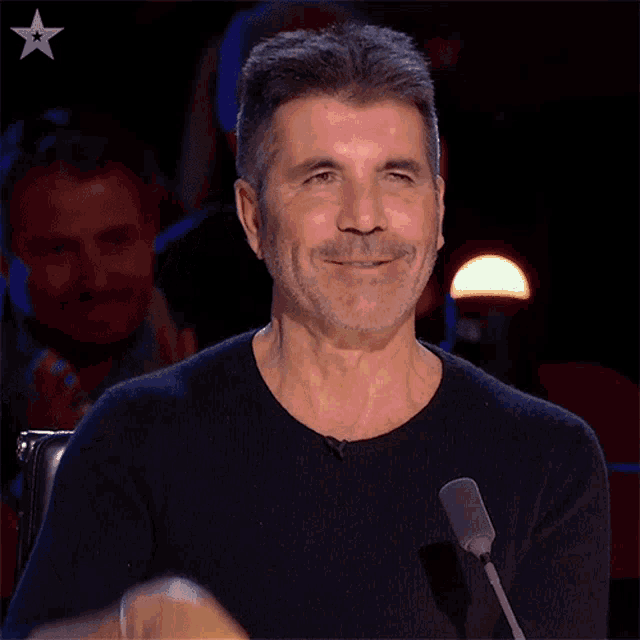 a man in a black shirt is smiling and holding his hand to his forehead