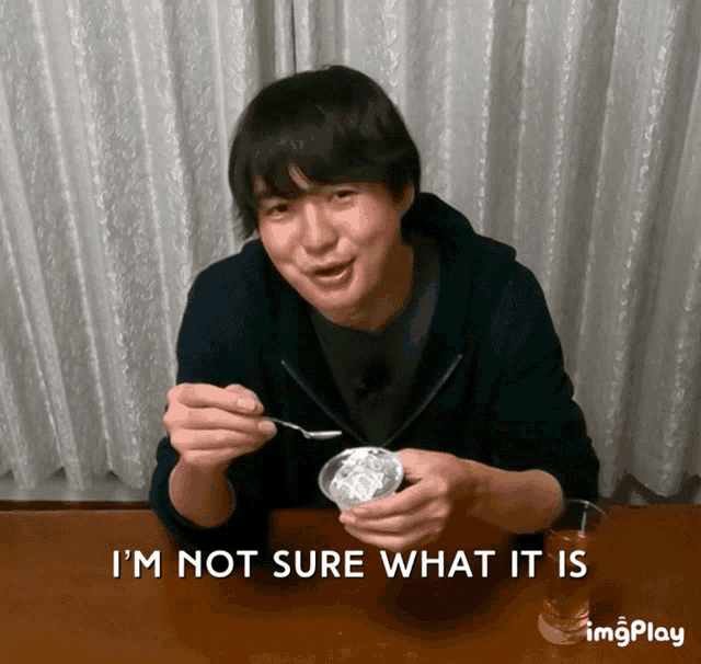 a man sitting at a table with a spoon in his mouth and the words " i 'm not sure what it is " above him