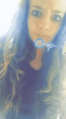 a woman with long blue hair is blowing bubbles in her mouth