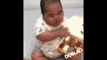 a baby is sitting on a bed with a box of food in his hands .