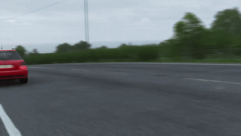 a red car is driving down a road with a license plate which says ' a ' on it