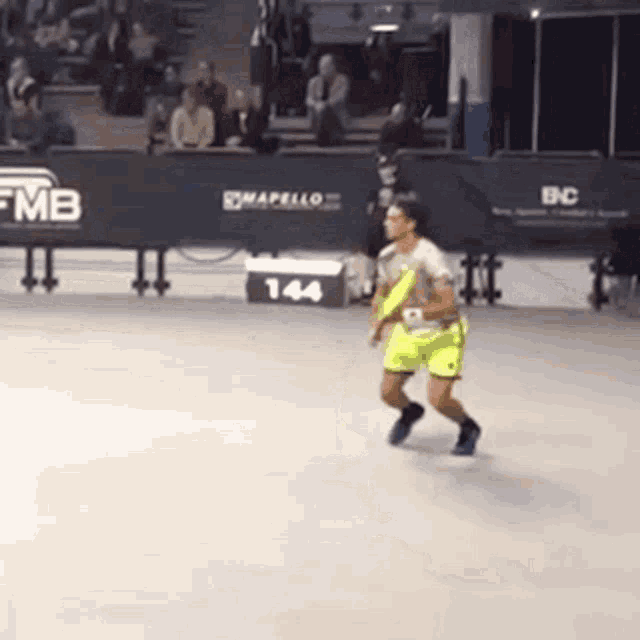 a man is running on a tennis court in front of a fence with the number 144 on it .