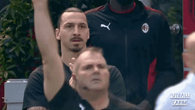 a man wearing a black puma shirt stands in a crowd