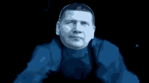 a man in a blue jacket is standing in the dark looking at the camera .