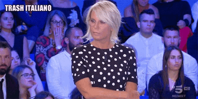 a woman in a black and white polka dot dress is standing in front of a crowd of people with trash italiano written on the bottom