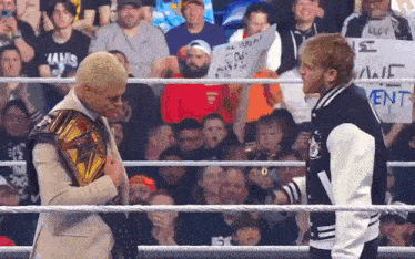 two men are standing in a wrestling ring and one of them is wearing a championship belt .