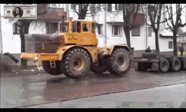 a yellow tractor is driving down a wet street with a dollar bill behind it