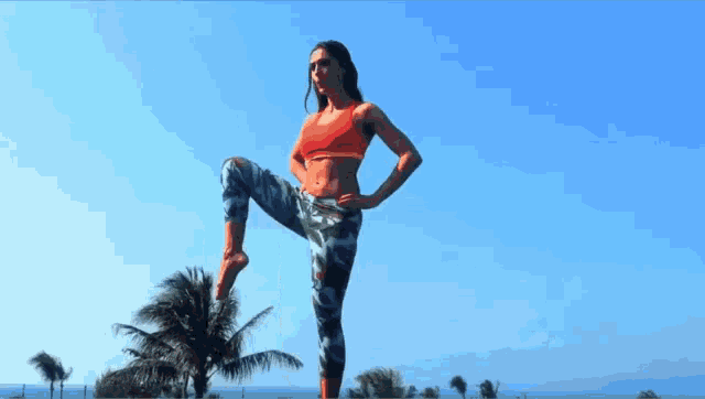 a woman in a red top and camo pants stands on one leg