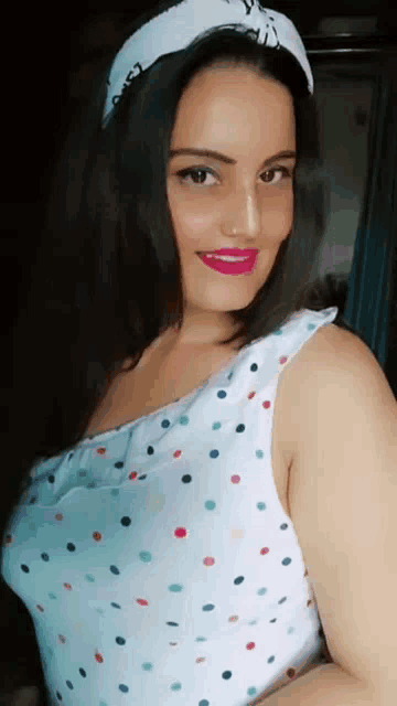 a woman wearing a white polka dot dress and a white headband is smiling .