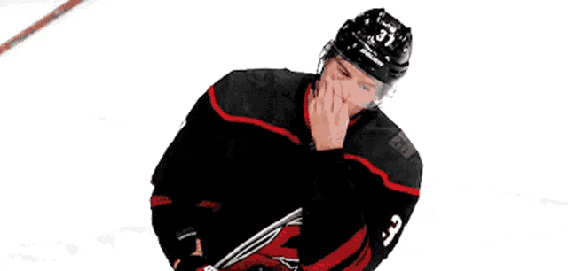 a hockey player wearing a black and red jersey and a helmet is standing on a rink .