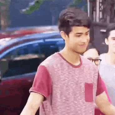 a young man wearing a pink shirt is standing in front of a red car