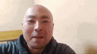 a bald man is looking at the camera while sitting in a chair .
