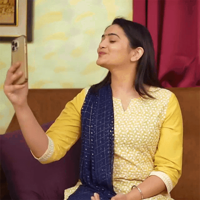 a woman in a yellow and blue dress is taking a selfie on her phone