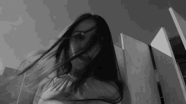 a black and white photo of a woman with long hair blowing in the wind .
