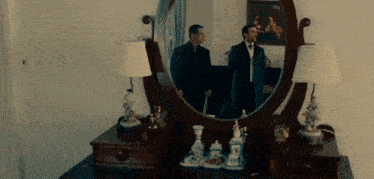 two men are standing in front of a mirror in a bedroom