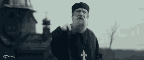 a man with a beard and a cross necklace is standing in front of a church .