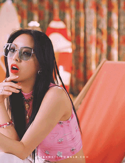 a woman wearing sunglasses and a pink crop top is sitting on a chair