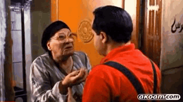 a man in a red shirt is talking to an older woman in a room .
