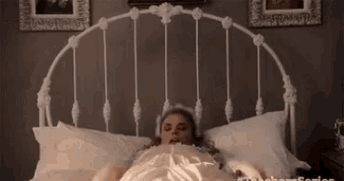 a woman is laying in a bed with a white headboard and white sheets .