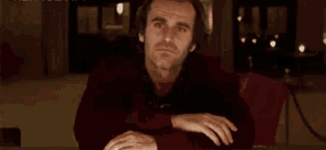 a man is sitting at a table laughing with his mouth open and his hands on his hips .