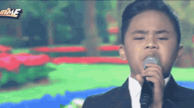 a young boy singing into a microphone with the word time on the bottom right
