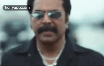 a man with a mustache and sunglasses is standing in front of a car .