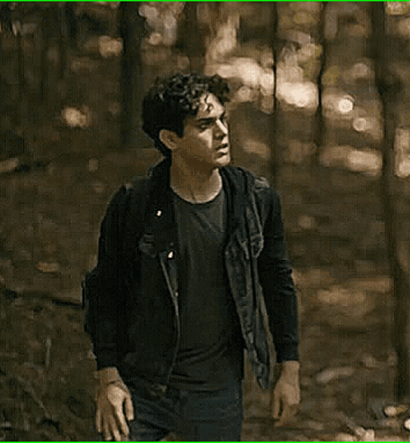 a man in a denim jacket is walking through a forest