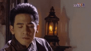 a man with his eyes closed is sitting in front of a lantern with the number 3 on it .
