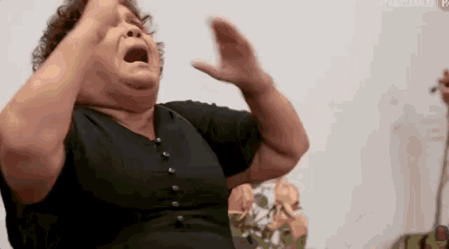 a woman in a black dress is sitting on a couch with her mouth open and her hands in the air .