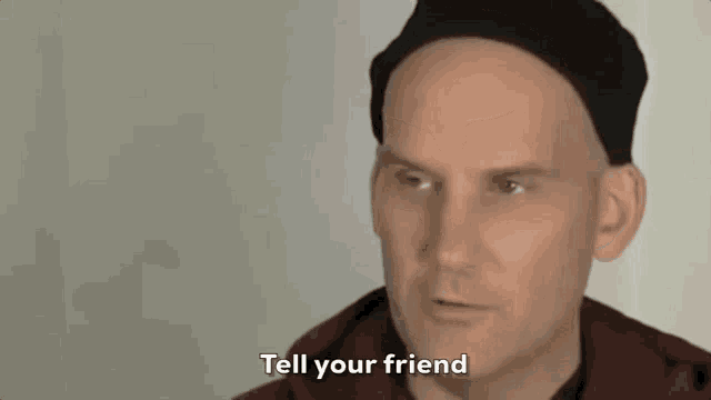 a bald man is wearing a black hat and talking to someone .