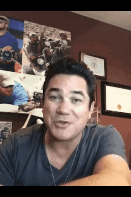 a man in a gray shirt is smiling in front of a wall of pictures