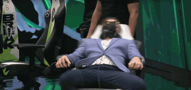 a man in a suit sits in a chair with a mercedes logo on the back