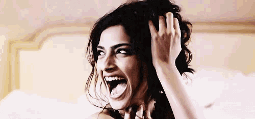 a woman is laughing and touching her hair while standing on a bed .