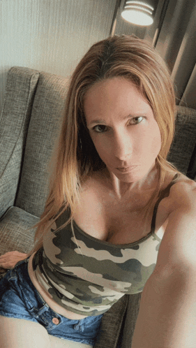 a woman sitting on a couch wearing a camo tank top